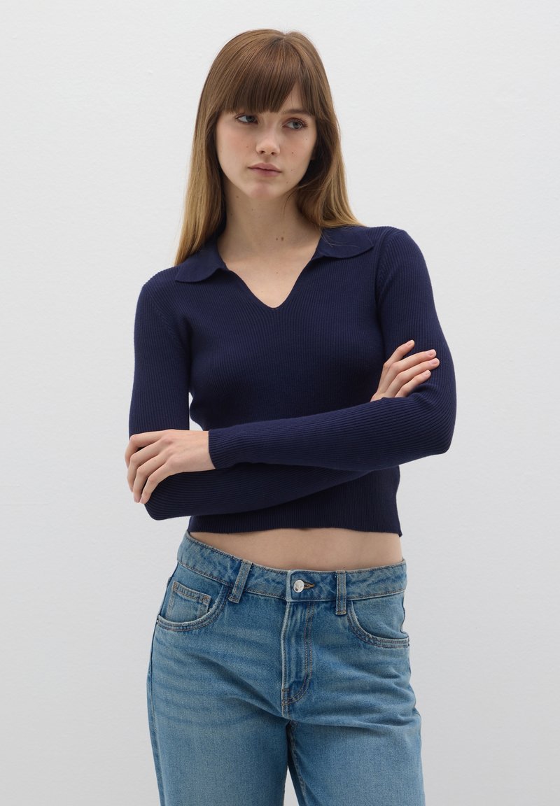 Suéter de punto acanalado en azul marino con un escote en V y cuello corto, combinado con jeans de talle alto en azul claro. El conjunto presenta un diseño cropped.