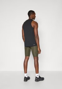 Top en algodón negro y pantalones cortos ajustados verde olivo, combinados con zapatillas deportivas negras y calcetines blancos, visto desde atrás.
