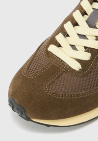 Brown suede sneaker featuring mesh panels, round toe, yellow laces, and a black rubber outsole with textured grip patterns.