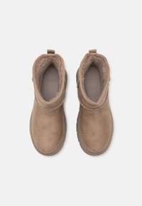 Par de botas de invierno de ante beige con forro de felpa, punteras redondeadas y pestañas en la parte trasera, vistas desde arriba sobre un fondo blanco.