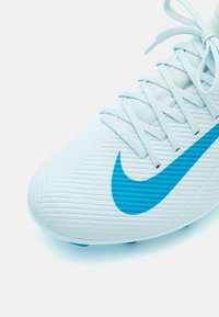 Scarpa da calcio bianca con swoosh blu di Nike. Presenta una superficie testurizzata con scanalature diagonali, lacci piatti e tacchetti rotondi sulla suola.