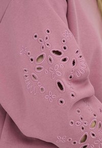 Felpa rosa con ricami floreali e dettagli con ritagli sulle maniche, caratterizzata da una texture morbida e una vestibilità casual.