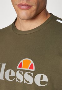 Olive green t-shirt made of cotton, featuring a large white logo with a multicolored semicircle design in orange and red accents.
