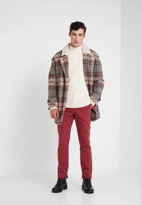 Abrigo de cuadros en gris, rojo y crema; suéter de punto crema; pantalones rojos; zapatos negros; tejido texturizado y detalle de cuello contrastante.