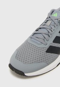 Grå sneakers med mesh-overdel, struktureret detaljering, sort stribe-logo, afrundet tå og gummisål. Har lysegrønne accenter.