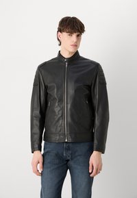 Black leather jacket with a high collar, zip front, and quilted shoulder accents. Features two side pockets and a sleek, fitted design.