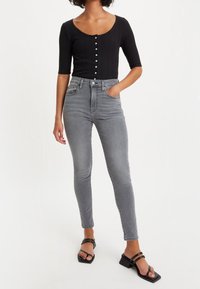Camisa negra de canalé con mangas cortas y botones en la parte delantera, combinada con unos jeans ajustados grises de cintura alta y sandalias negras de tiras.