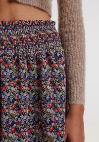 Bloemenrok met een gestikte tailleband, met levendige kleuren zoals rood, blauw en groen, op een donkere achtergrond van een zachte, textuurstof.