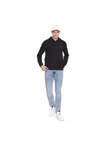 Sudadera negra con bolsillo frontal, combinada con jeans de mezclilla azul claros y zapatillas blancas. El hombre lleva puesto un gorra de béisbol blanca, de pie en una pose neutral.