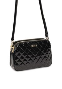 Borsa a tracolla in pelle verniciata nera con design trapuntato, dettagli in oro sulla cerniera e una tracolla sottile regolabile.