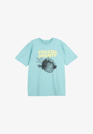 Jasnoniebieska koszulka z żółtym napisem "COASTAL ANXIETY" oraz czarną ilustracją rozdymki z napisem "GDZIEŚ BLISKO OKINAWY."