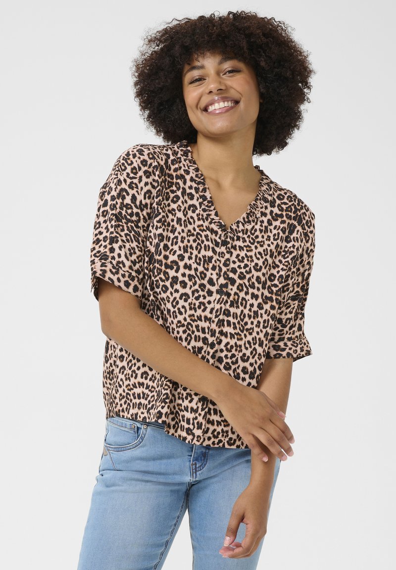 Blusa a maniche corte con stampa leopardata, scollatura a V e dettagli arricciati, realizzata in tessuto morbido. Abbinata a jeans in denim azzurri.