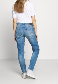 Jeans de mezclilla azul ajustados con una cintura de altura media, un ligero desgastado y bolsillos traseros. Combinados con zapatillas blancas y una camiseta blanca.