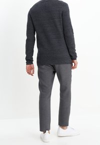 Dunkelgrauer Strickpullover mit langen Ärmeln, kombiniert mit hellgrauen schlanken Hose und weißen Sneakern, von hinten betrachtet.
