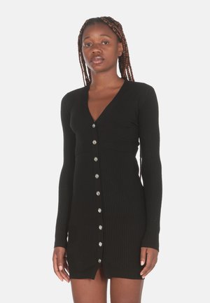 Abito nero a coste con maniche lunghe, scollatura a V e dettagli con bottoni argentati lungo il davanti. Design aderente con orlo a metà coscia.