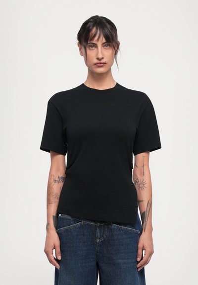 Svart bomull t-skjorte med korte ermer, rund hals og avslappet passform. Brukt sammen med denimjeans, med synlige arm-tatoveringer.