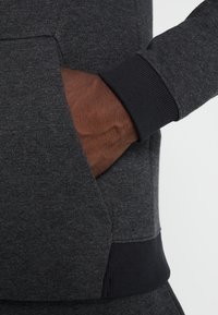 Sudadera gris oscuro con un acabado texturizado, que cuenta con un bolsillo canguro y puños acanalados en negro contrastante.