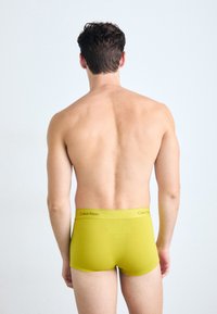 Rumene bombažne bokserice brez vzorca z elastičnim pasom, ki nosi blagovno znamko "Calvin Klein" v kontrastni barvi.