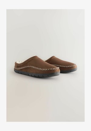 Ruskosuede-nilkkasukat, joissa on vaalea tekoturkisvuori, kontrastoiva valkoinen ommel yläosassa ja teksturoitu musta kumipohja.