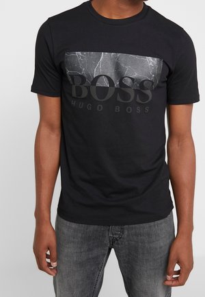 Schwarzes Baumwoll-T-Shirt mit einem Marmor-Muster über der Brust, auf dem "BOSS" in fetten grauen Buchstaben und "HUGO BOSS" darunter in kleinerer Schrift gedruckt ist.