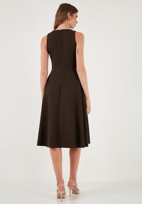 Brązowa sukienka bez rękawów z dopasowanym stanem i rozkloszowanym dołem. Posiada zamek błyskawiczny z tyłu i gładką teksturę. Połączona z cielistymi sandałami na wysokim obcasie.