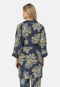 Kimono floreale in tessuto blu scuro con motivi floreali gialli e blu, maniche a tre quarti e cintura legata in vita.