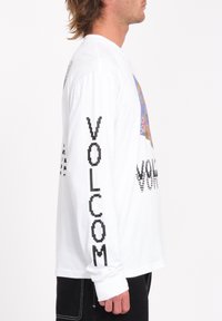 Langærmet hvid bomulds T-shirt med et farverigt grafisk tryk på fronten og "VOLCOM" trykt i sort på begge ærmer.