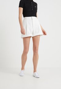 Vita skräddarsydda shorts med uppvikta ben, med dragkedja framtill och plisserade detaljer. Kombineras med en svart polo och vita sneakers.