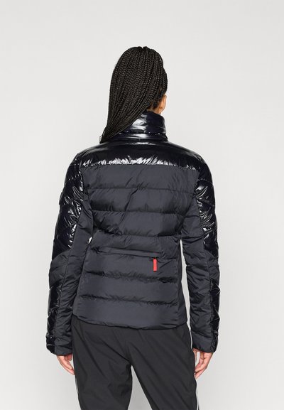 Φουσκωτό μπουφάν σε ναυτικό μπλε με γυαλιστερή φινιρίσματα, που διαθέτει κεντημένες τμήματα, ψηλό γιακά και κόκκινη τσέπη με φερμουάρ στο πίσω μέρος.