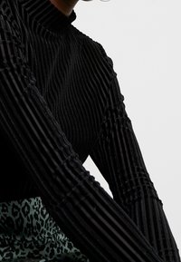 Schwarz gestreifter Rollkragenpullover aus strukturiertem Stoff, mit vertikalen Rillen und einem körperbetonten Design. Der untere Teil zeigt ein grünes Leopardenmuster.
