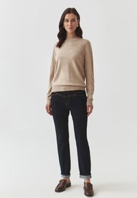 Beige gebreide trui, donkerdenim jeans met opgerolde manchetten en bruine loafers. Heeft een relaxte pasvorm en een minimalistisch ontwerp.