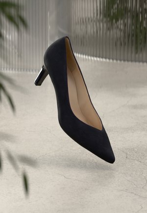 Black suede pump with a pointed toe and a low glossy heel. The shoe has a smooth interior, emphasizing a sleek and modern design.