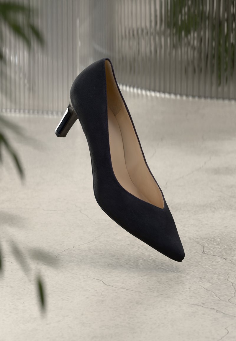 Escarpin en suede noir avec un bout pointu et un petit talon brillant. La chaussure possède un intérieur lisse, mettant en avant un design épuré et moderne.