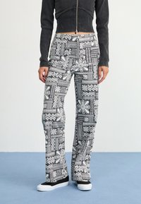 Black and white patterned flared pants feature geometric designs and floral shapes. Made from a lightweight fabric with a smooth texture.