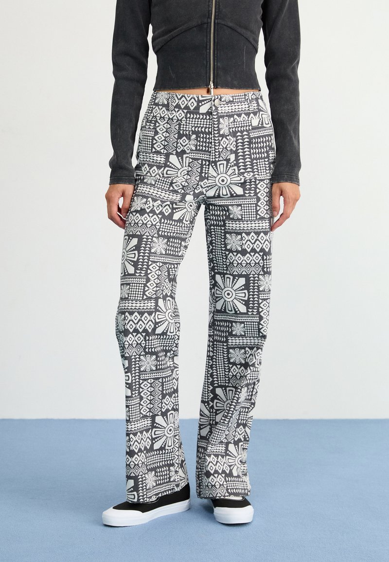 Black and white patterned flared pants feature geometric designs and floral shapes. Made from a lightweight fabric with a smooth texture.