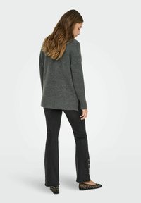 Pull en tricot gris à coupe décontractée. Doté d'un ourlet et de poignets côtelés. Associé à un jean noir évasé avec des boutons sur le côté, et des ballerines noires.