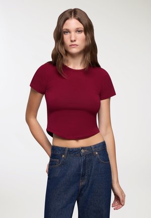 T-shirt bordeaux corto con scollatura rotonda abbinato a jeans blu a vita alta. Il tessuto sembra liscio e aderente.