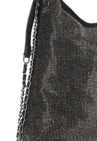 Zwarte geweven handtas met een getextureerd oppervlak, voorzien van metalen studs, een kettingriem en een zachte stoffen bovenrand.