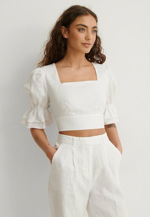Biele ľanové crop top s štvorcovým dekoltom a vypchatými rukávmi. Skombinované s bielymi ľanovými nohavicami s vysokým pásom a bočnými vreckami.