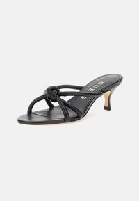 Sandale à talons noirs avec une finition en cuir lisse. Présente des brides entrelacées, un accent noué et un talon mince et courbé.