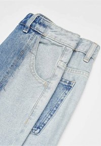 Jeans bleu clair avec un design de couleurs mélangées, présentant un délavage sur un côté et une teinte uni de l'autre. Comprend des poches avant.