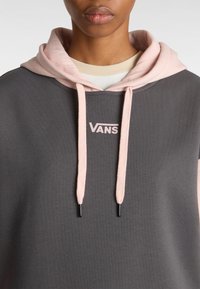 Tmavě šedá mikina s kapucí s vnitřní výstelkou světle růžové barvy, na které je malé bílé logo "VANS" a stahovací šňůrky se černými konci.