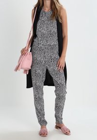 Czarny i biały kombinezon w wzory z bezrękawnikowym krojem, zestawiony z długim czarnym kardiganem, różową torebką oraz dobranymi klapkami.