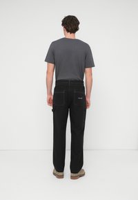 Μαύρο παντελόνι φορτίου με πολλ ές τσέπες, αντίθετη ραφή και χαλαρή εφαρμογή, σε συνδυασμό με γκρι κοντομάνικη μπλούζα.