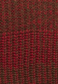 Strickstoff in tiefen Rot- und Brauntönen, mit einem strukturierten Zickzackmuster, sichtbaren Fasern und einer dichten Webart.