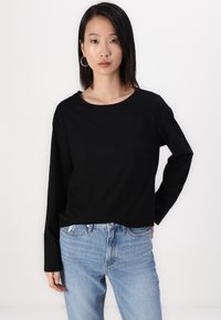 Svart langermet topp med rund hals, laget av myk stoff. Sammen med lys blå jeans som har en avslappet passform og synlig søm.