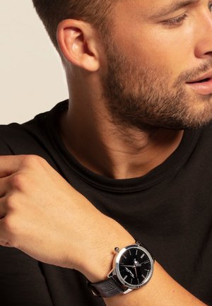 Montre avec bracelet en cuir noir, boîtier en acier inoxydable argenté, cadran noir, index des heures argentés et un design minimaliste.