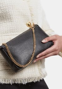 Borsa a tracolla nera in pelle con una finitura testurizzata, dotata di una catena dorata e di un dettaglio a chiusura rotonda.