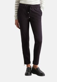 Zwarte joggpants met een tailleband met trekkoord, getailleerde pasvorm, zijzakken en ritsen bij de enkels. Glad stofmateriaal.