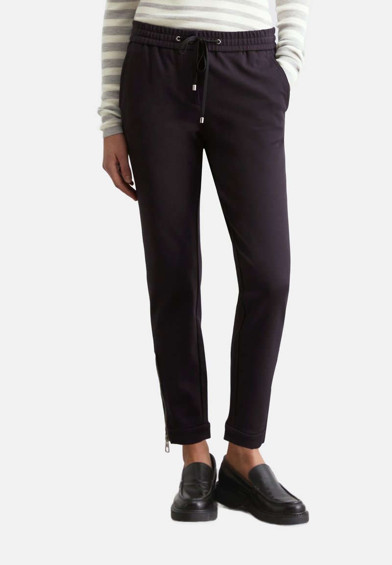 Zwarte joggpants met een tailleband met trekkoord, getailleerde pasvorm, zijzakken en ritsen bij de enkels. Glad stofmateriaal.